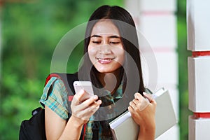 Smiling asian student holding book and reading text message