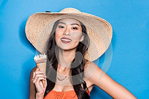 smiling asian woman in beach attire holding an ice-cream cone and looking