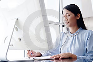 Smiling Asian woman is call center or secretary operator is wearing a headset and a microphone for consultant to customers.