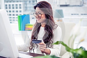 Smiling Asian woman on computer holding credit card