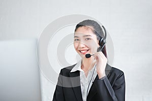 Smiling Asian woman consultant wearing microphone headset of customer support phone operator at workplace.