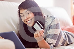 Smiling asian woman on couch using tablet to shop online