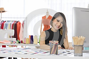 Smiling Asian woman dressmaker is sitting  sketch dress that she has to cut for the customer in the Tailor shop and sewing