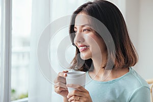 Smiling asian woman drinking coffee relaxing on the couch at home