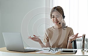 Smiling asian woman freelancer wearing headset, communicating with client via video computer call. Millennial pleasant