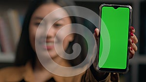 Smiling asian woman girl holding smartphone showing new application close-up green empty screen gadget mobile phone