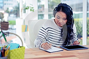 Smiling Asian woman with headphones writing on notepad