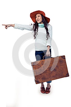 Smiling Asian woman holding luggage pointing somewhere