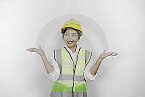 A smiling Asian woman labor wearing safety helmet and vest, pointing to copy space beside her, isolated by white background. Labor