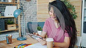 Smiling Asian woman office worker using tablet at work touching screen