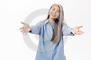 Smiling asian woman reaching hands. Old senior lady stretching out arms forward, welcome, standing over white background