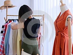 Smiling Asian woman Selecting clothes in the Tailor shop of fabrics store. Fashion designer standing look at dress in the clothing