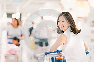 Smiling Asian woman with shopping cart or trolley at department store or shopping mall