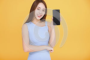 Smiling asian woman showng mobile phone screen on yellow backgroundi