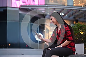 Smiling woman sitting on bench in a city and using smart phone.