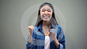 Smiling asian woman with smartphone doing yes gesture, giveaway winner, luck