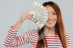 Smiling asian woman in sweater is covering in money