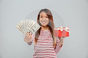 Smiling asian woman in sweater holding money and gift