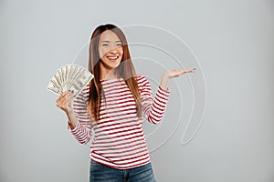 Smiling asian woman in sweater showing money and holding copyspace