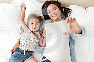 Smiling asian woman taking selfie with her little daughter