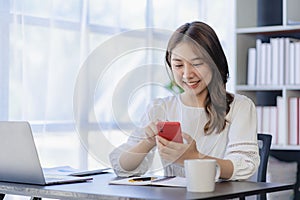 Smiling Asian woman talking on the phone with a customer Young positive female accountant using smartphone talking