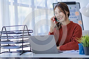 Smiling Asian woman talking on the phone with a customer Young positive female accountant using smartphone talking