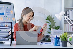 Smiling Asian woman talking on the phone with a customer Young positive female accountant using smartphone talking