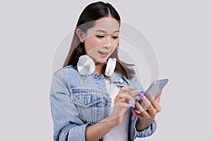 Smiling Asian woman using an application to listen to music on her phone. She wears bluetooth headphones