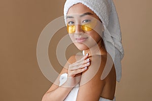 Smiling Asian woman using gold under-eye patches after shower