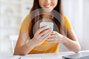 Smiling asian woman using her smartphone, texting or browsing internet at home