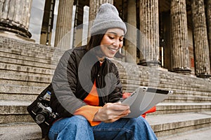 Smiling asian woman using tablet computer while sitting on stairs at old city street