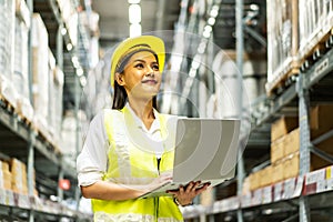 Smiling asian woman warehouse worker doing stocktaking of products management in cardboard box on shelves in warehouse