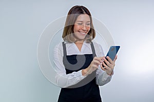 Smiling Asian woman in wearing apron typing sms messages in mobile phone