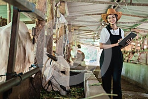 smiling Asian woman wearing a cowboy hat looks at the camera while carrying a pad