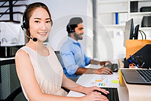 Smiling Asian woman working as customer support operator with headset in a call center. Portrait of sales agent sitting at desk