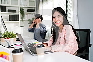 Smiling Asian woman working as customer support operator with headset in a call center. Portrait of sales agent sitting at desk