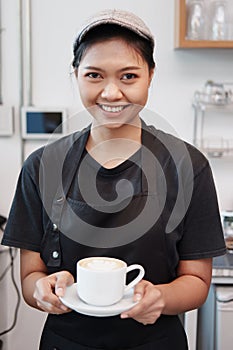 Smiling Asian Young barista woman is hand holding a cup  of hot coffee at counter in cafe. Start up for Coffee shop and cafe