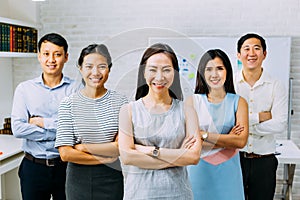 Smiling Asian young business people in casual wear standing in line with arms folded in meeting room