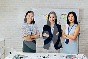 Smiling Asian young business women in casual wear standing in line with arms folded in meeting room