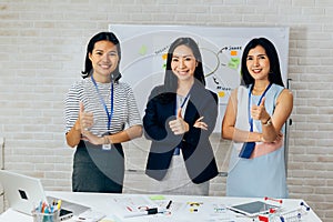 Smiling Asian young business women in casual wear standing in line with thumbs up gesture in meeting room