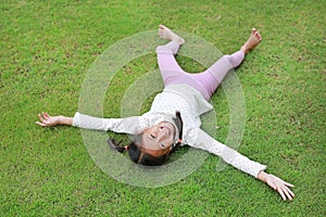 Smiling Asian young girl child lying on green lawn at the garden. Kid lies on grass with looking camera