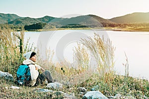 Smiling Asian young man backpackers sitting on the grass in mountains, river enjoying their alone outdoor active. lifestyle travel