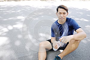 Smiling Asian young man in navy blue sportwear Thirsty and drinking water in bottle after exercise and running.