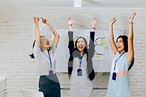 Smiling Asian young and mature business women standing in line with arms raised up gesture in meeting room with excited