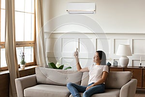 Smiling Asian young woman using air conditioner remote controller