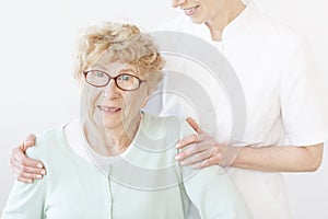 Smiling assistant hugging old lady