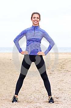 Smiling athlete standing on beach with hands on hips