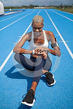 Smiling athletic sportswoman touch a smart watch, wears earphones of smartphone in armband. Tracks her running sports training and