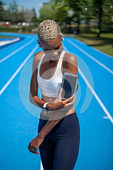 Smiling athletic sportswoman wears earphones and touch smartphone in her armband. Tracks her running sports training and jogging.