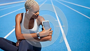 Smiling athletic sportswoman wears earphones and touch smartphone in her armband. Tracks her running sports training and jogging.